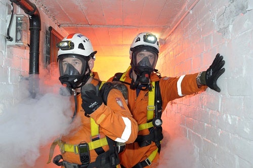 Two people wearing breathing apparatus in a confined space where there is smoke