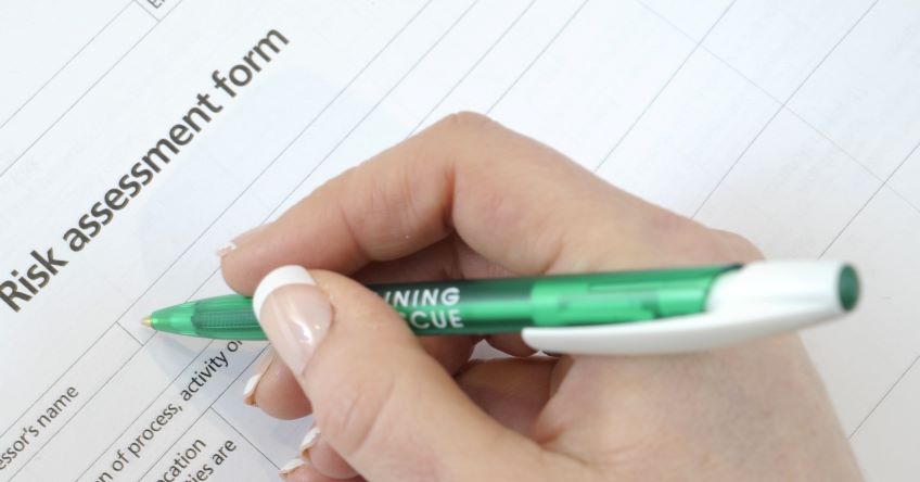 A hand holding a pen filling in a risk assessment form 