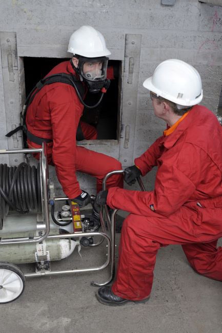 Two rescuers entering a confined space wearing red safety apparel and airline breathing apparatus.
