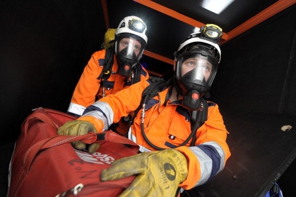 Two men in safety work wear and breathing apparatus in a confined space
