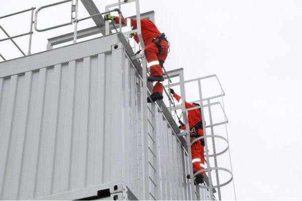 Two people wearing orange high-vis suits are on top of scaffolding, as part of the MRS Rooftop Safety Training course 