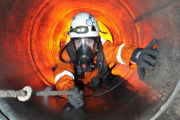 Man in enclosed tunnel holding on to rope in full safety breathing apparatus - confined space