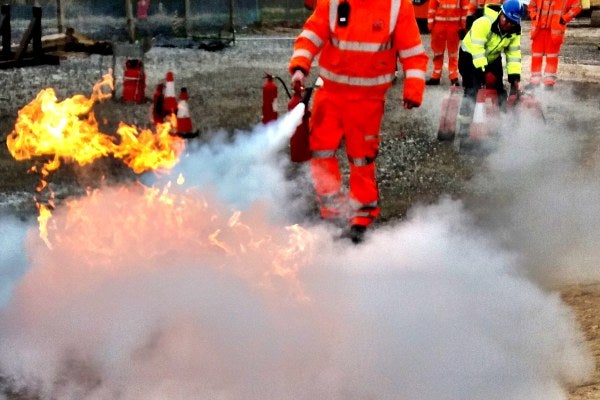 A group of people are taking part in the wind turbine Fire Awareness course, practicing to put out a fire. 
