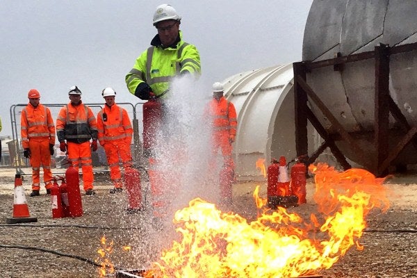 A group of people in high-vis gear are watching an MRS Fire Awareness instructor put out a fire.