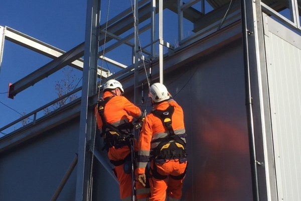 Two people wearing orange high-vis suits are on top of scaffolding, as part of the MRS Advanced Working & Rescue From Height Training Course.