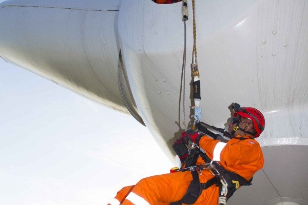 A person is scaling a wind turbine with PPE, as part of their Working at Height and Rescue Wind Turbine Refresher Training. 