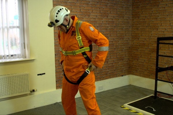 Man stood wearing safety work wear and putting on a harness