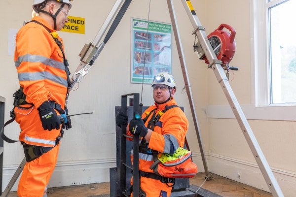 Man wearing protective clothing standing near tripod at top of confined space entry point