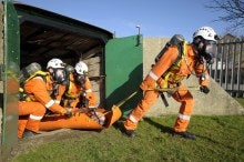 3 members of a rescue team removing a casualty from a confined space on a ground stretcher