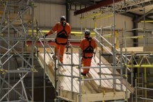 Three people are in a dark space wearing high visibility clothing and hard hats with lights on